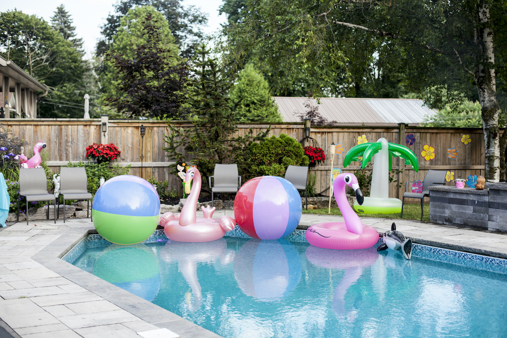 An inviting backyard pool full of hawaiin themed toys. pool fence