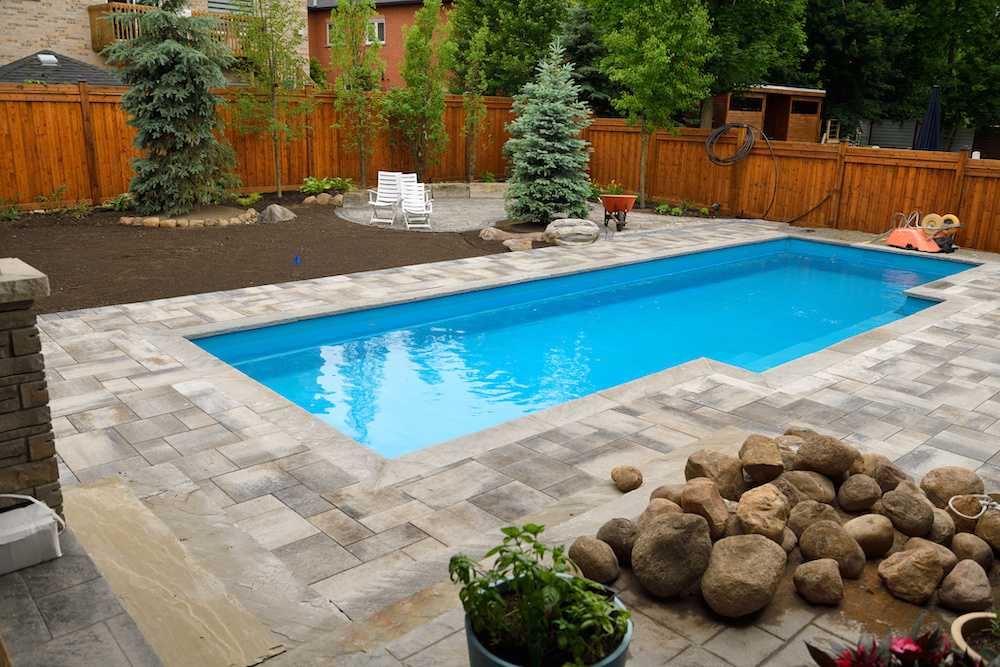 Newly installed swimming pool in Spring with unfinished, back yard landscaping construction ongoing fence for backyard pool